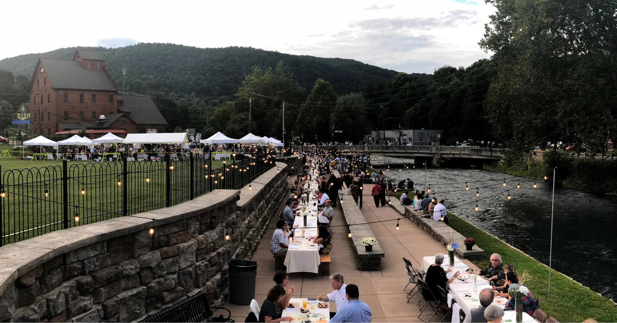 A long community dinner table set along the creek in downtown Bellefonte at dusk.